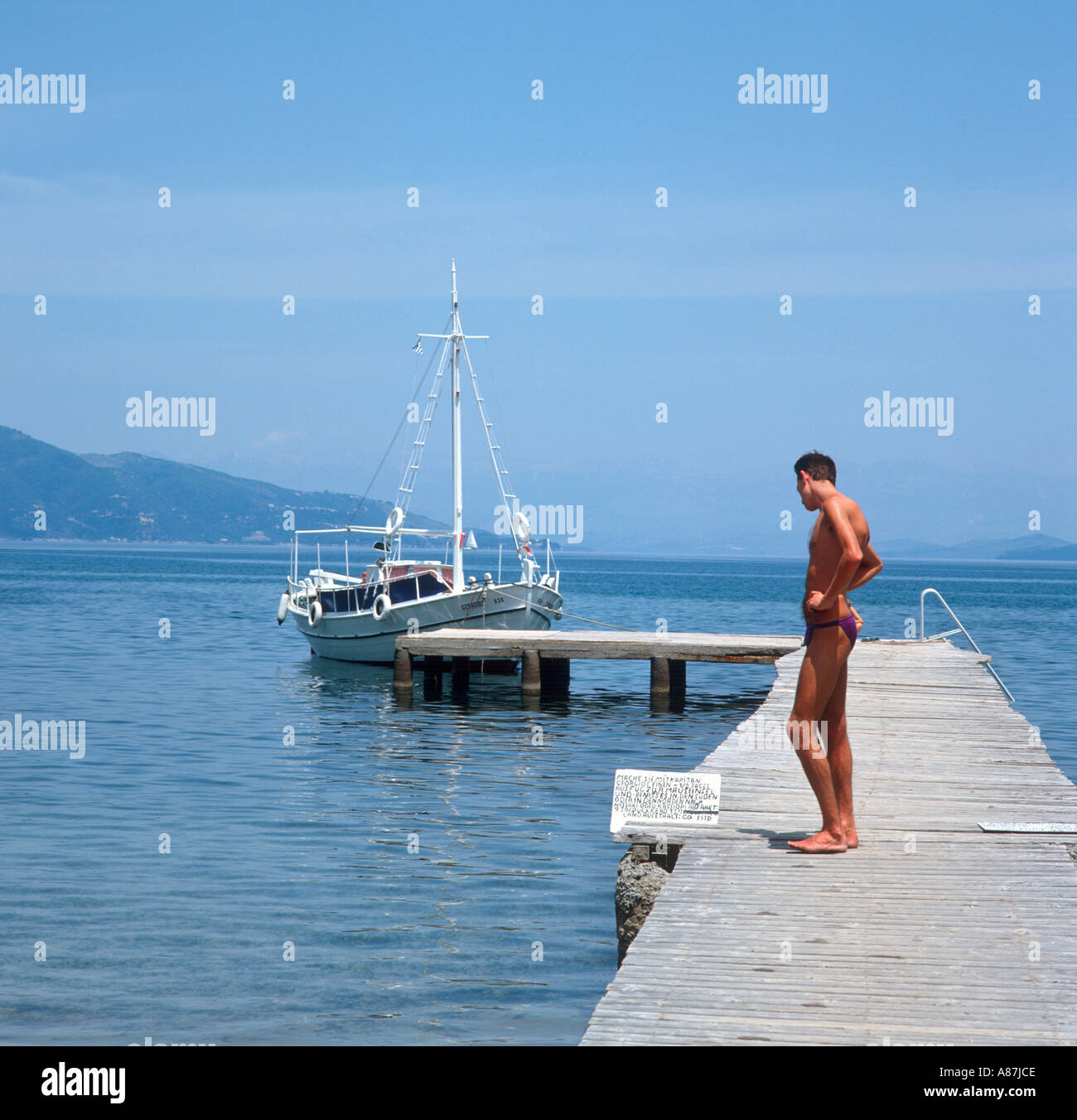 Mann auf der Anlegestelle in Alykes mit einem Ausflugsschiff hinter Korfu (Kerkyra), Ionische Inseln, Griechenland Stockfoto