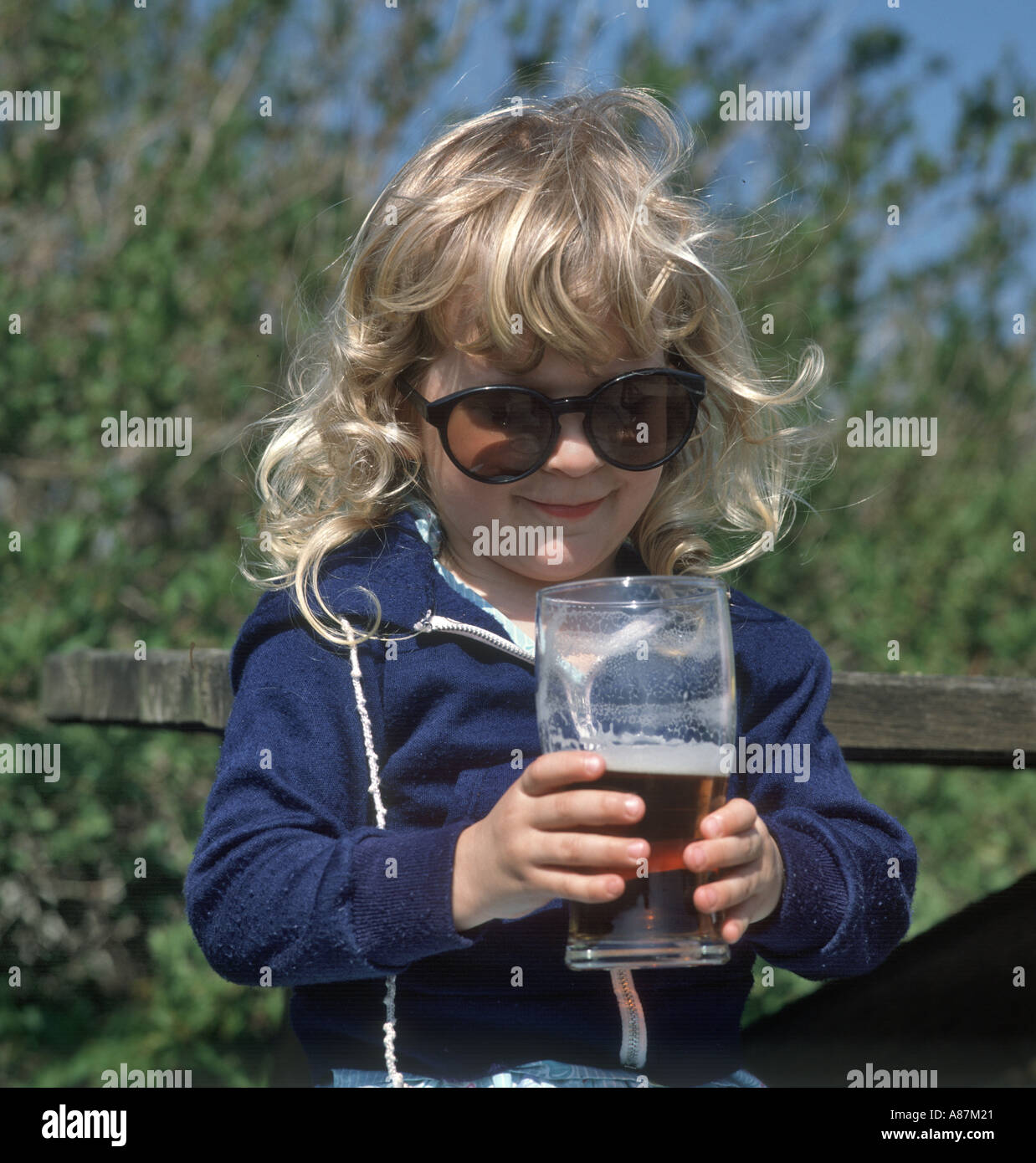 Kleines Mädchen versucht, trinken Sie einen Pint Bier und tragen übergroße Sonnenbrille, England, Vereinigtes Königreich Stockfoto
