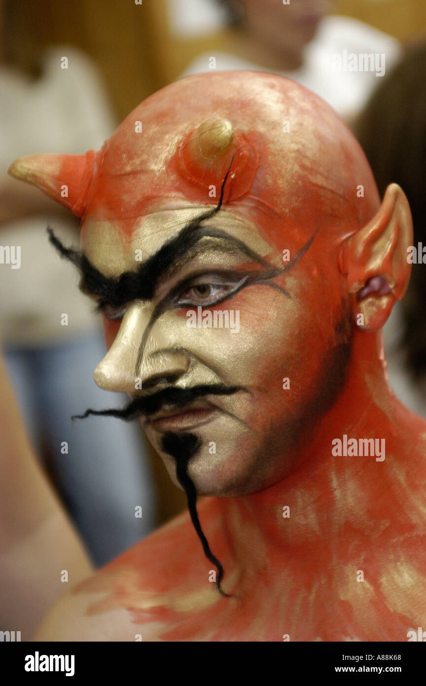 Männlicher gehörnter Teufel mit roter und goldener Gesichtsfarbe, spitzen Ohren, langem schwarzen Schnurrbart und edlem Bart. Stockfoto