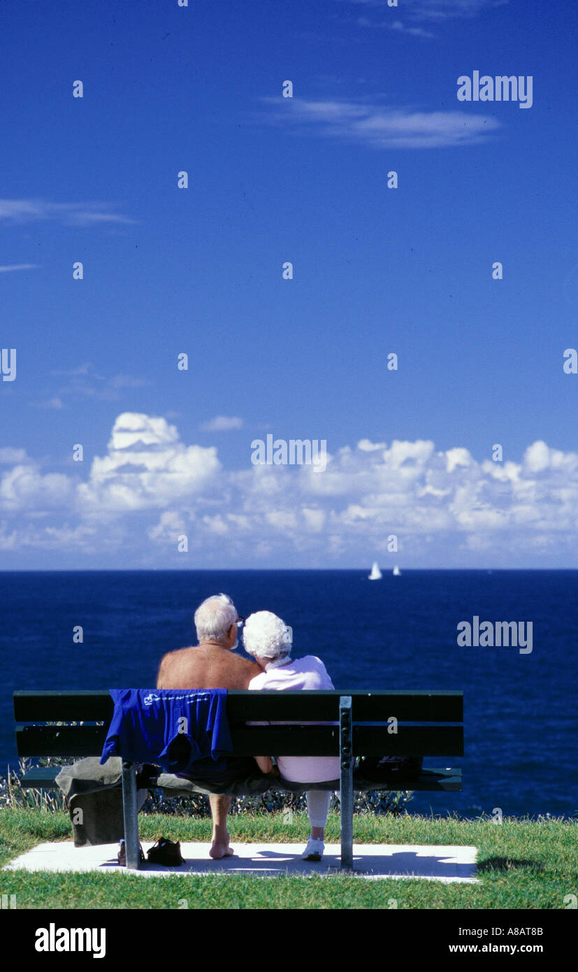 Altes Ehepaar sitzen und schauen auf einen Blick über einen schönen Blick aufs Meer und blauer Himmel Tag mit Wolken und Yachten Segeln Stockfoto