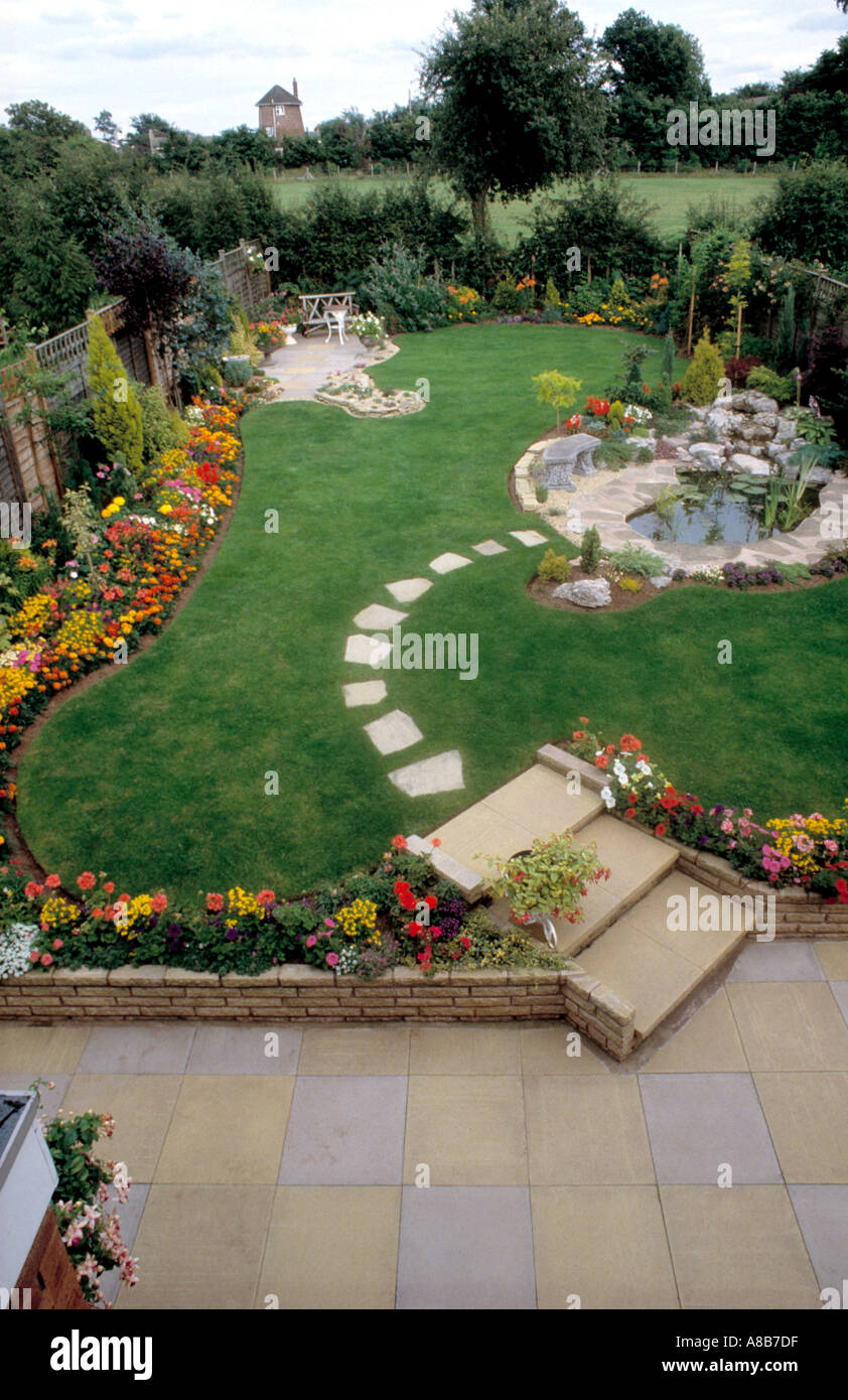 Birdseye-Ansicht der gepflasterten Terrasse und Rasen mit gepflasterten Weg zum Teich im Garten s-Stil mit bunten Sommerblumen Stockfoto