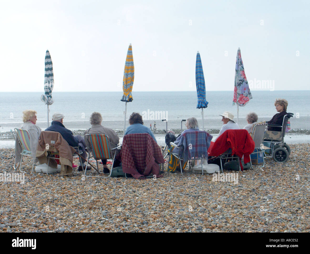 Worthing West Sussex Gruppe von Senioren sitzt am Strand vielleicht pessimistisch, dass sein Gehen, Regen & gefaltet Sonnenschirme Sonnenschirme könnte Großbritannien geworden Stockfoto