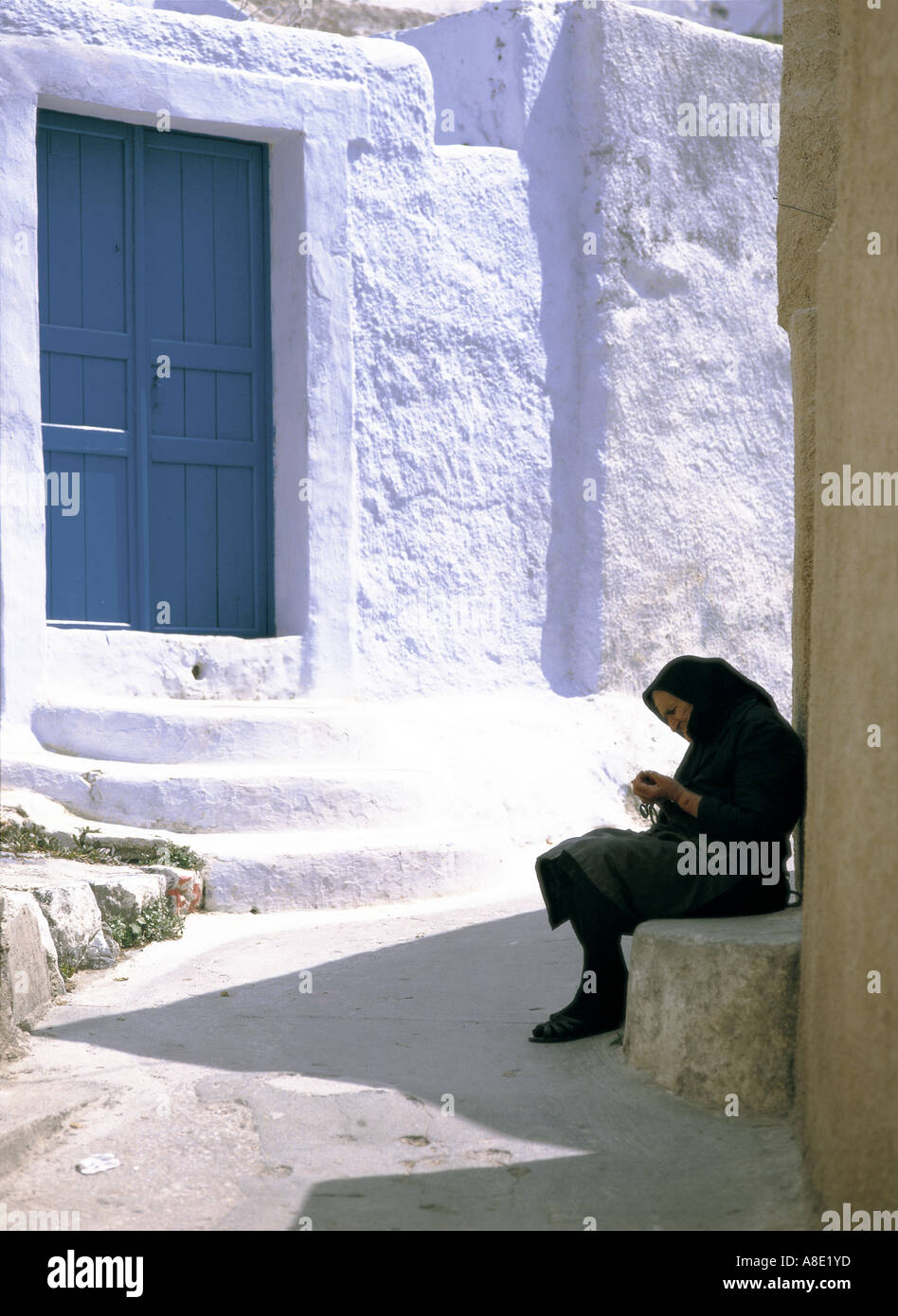 Alte Frau in schwarzer Tracht sitzen bei Street, Santorin, Griechenland Stockfoto