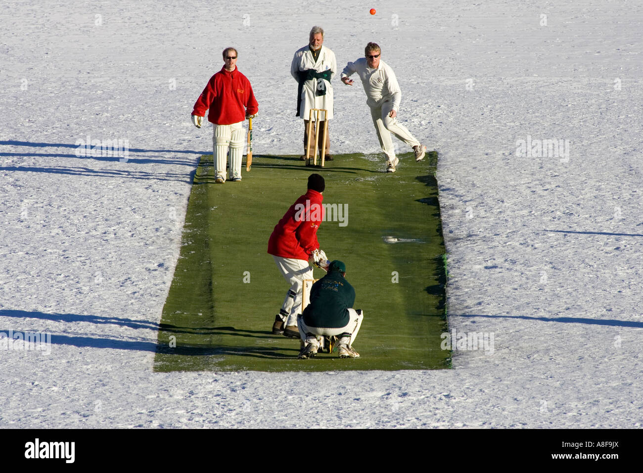 Ein Bowler Uhren seinen Ball durch die Luft auf die Stümpfe im Cricket on Ice St. Moritz in der Schweiz abfliegen. Stockfoto