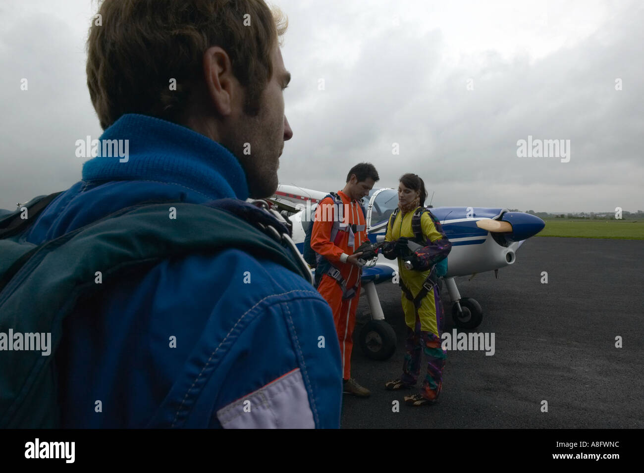 Drei Personen tragen Fallschirm Ausrüstung außerhalb in der Nähe von Flugzeug im Gespräch Stockfoto