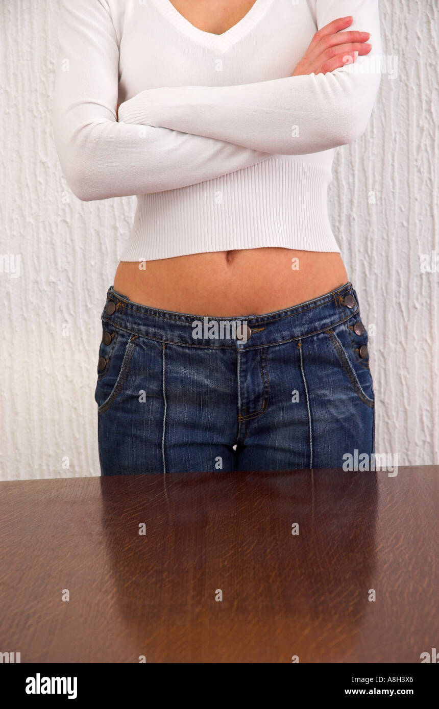 Junge Frau am Tisch mit ihren verschränkten Armen Stockfoto