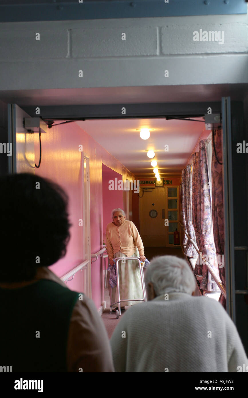 Ältere Bewohner zu Fuß durch einen Korridor mit Hilfe in einem Pflegeheim für asiatische Senioren, Aashna House, London, UK. Stockfoto