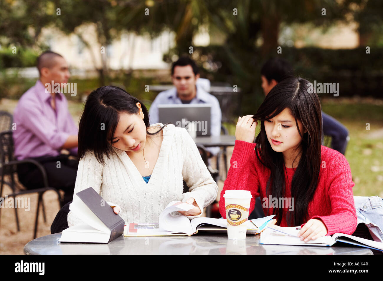 Zwei junge Frauen studieren in einem Uni-Campus mit drei junge Männer sitzen im Hintergrund Stockfoto