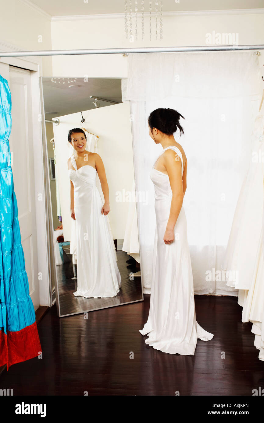 Junge Frau trägt eine Hochzeitskleid und betrachtet sich im Spiegel Stockfoto