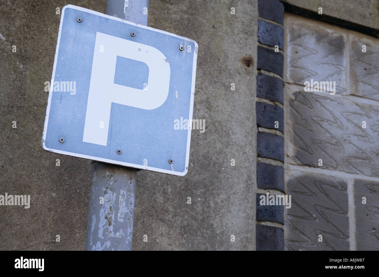 Blaue und weiße P oder Zeichen auf einem Mast oder Lampe Pfosten von einem schmuddeligen Zement und Brise Blockwand Parken Stockfoto