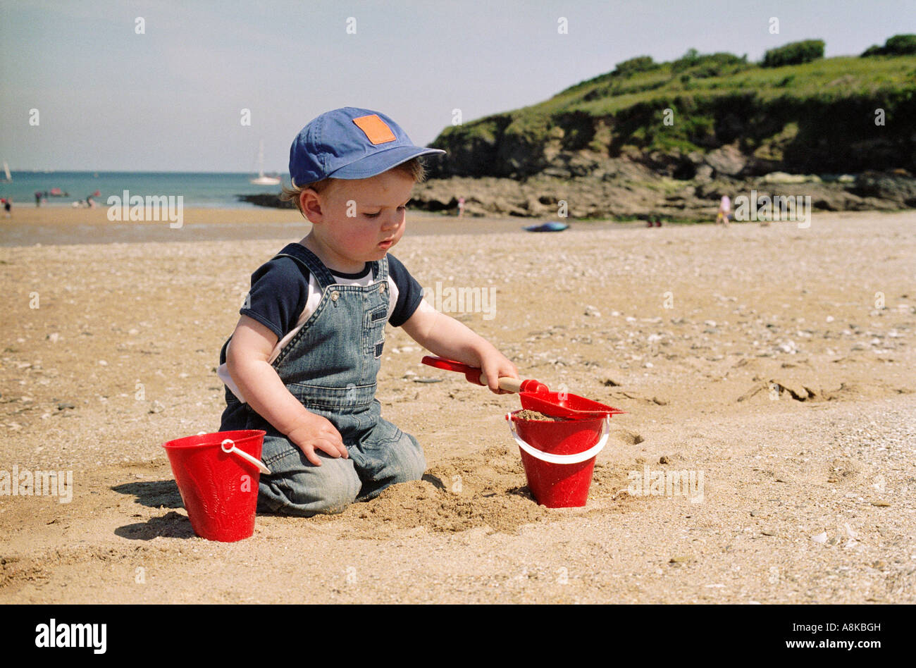 Ein junges Kind spielen am Strand mit zwei roten Eimer und Spaten Stockfoto