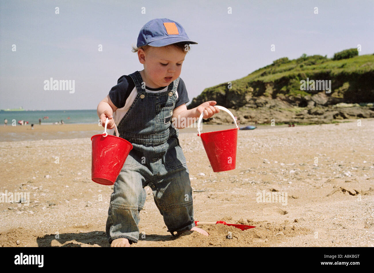 Ein kleines Kind mit zwei roten Eimer voll sand Stockfoto