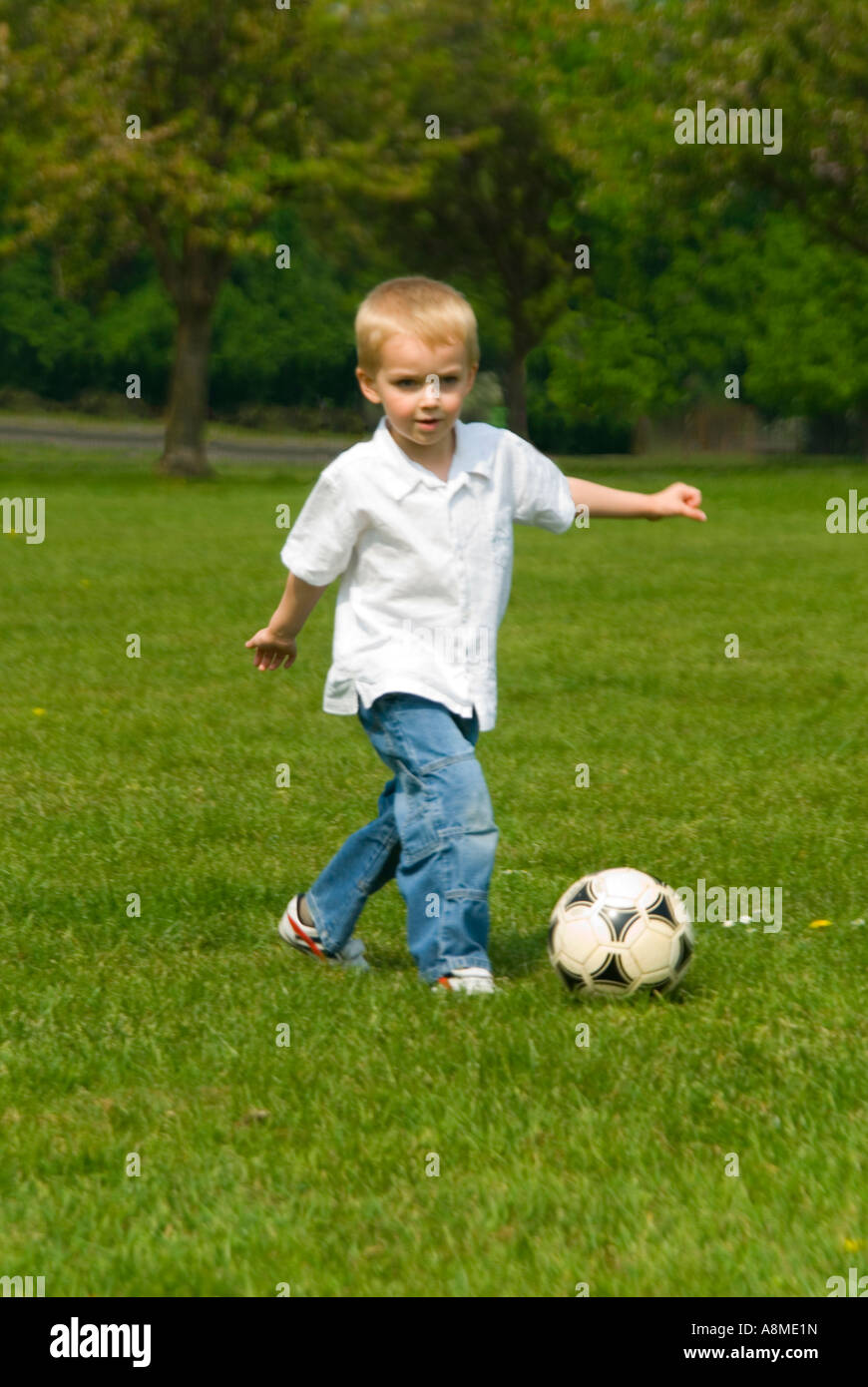 Vertikale Porträt eines jungen Mannes (4 Jahre alt) treten einen Fußball während eines Spiels im Park an einem sonnigen Frühlingstag Stockfoto