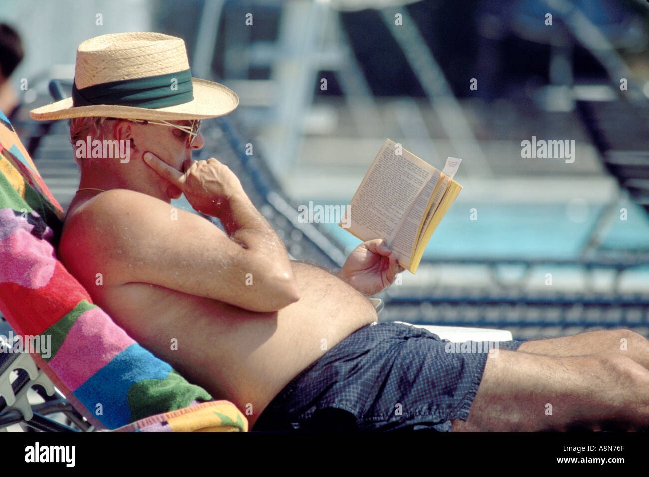 Älterer Mann lesen und bekommen eine tan an Club Pool mit Stroh hatte Stockfoto
