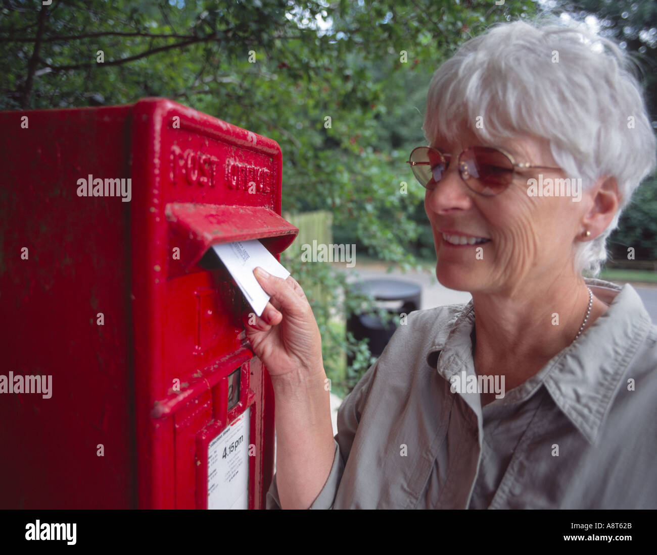 ältere Frau Entsendung einen Brief in traditionellen roten britischen Brief box im Land Stockfoto