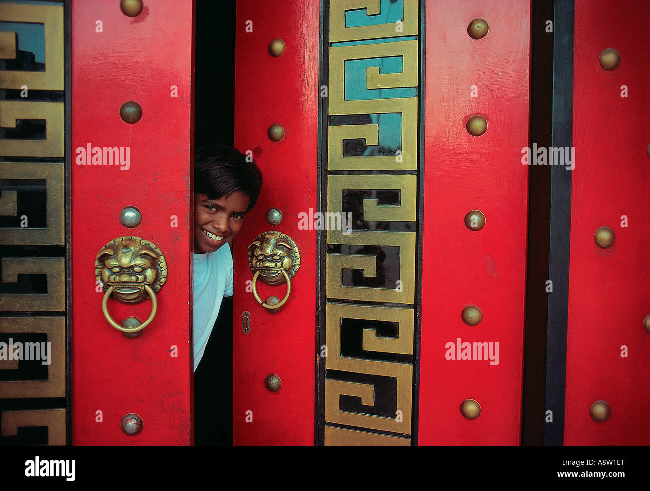 Singapur. Ein einheimischer Junge, der durch die imposanten roten Doppeltüren hinausschaut. Stockfoto