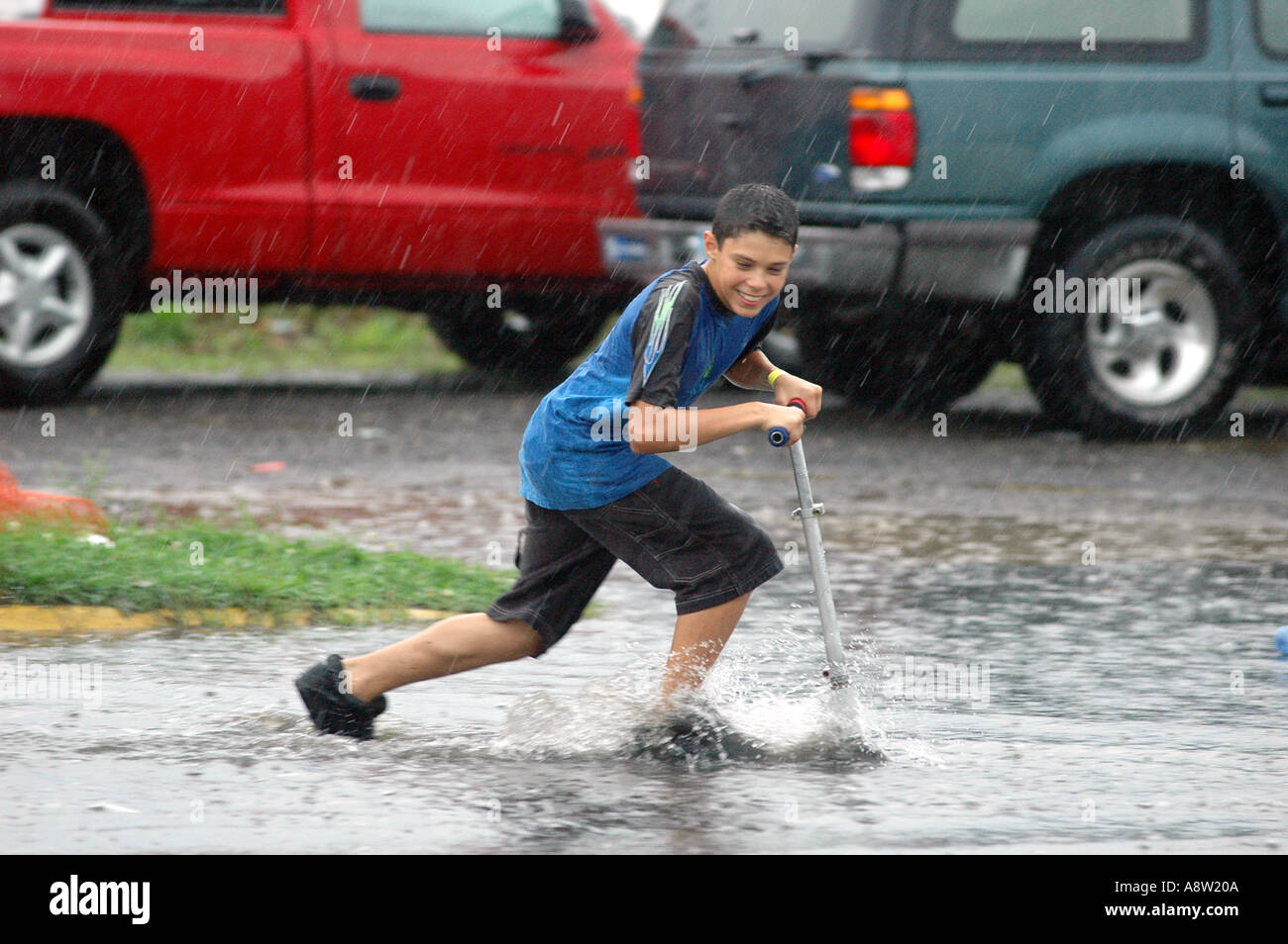 Junge Reiten Roller Skateboard durch überflutete Wasserpfütze Stockfoto