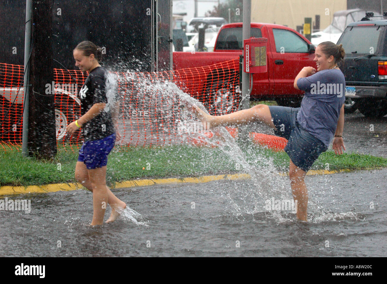 Zwei Teen Girls spielen in überfluteten Straßen mit Spritzwasser einander nach starken Regenfällen Stockfoto