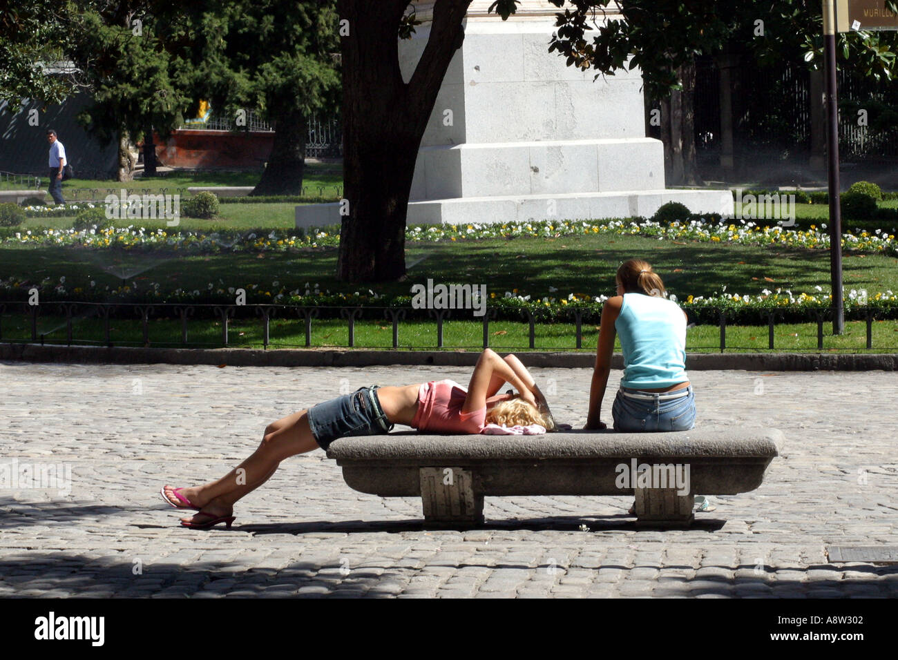 Zwei Mädchen entspannen in der Sonne auf einer Parkbank in Madrid Spanien Stockfoto