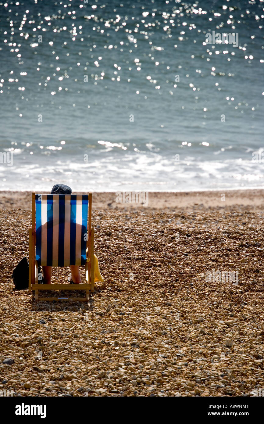 Person sitzt in einem hinterleuchteten Liegestuhl am Strand in Eastbourne, Sussex, England, UK Stockfoto