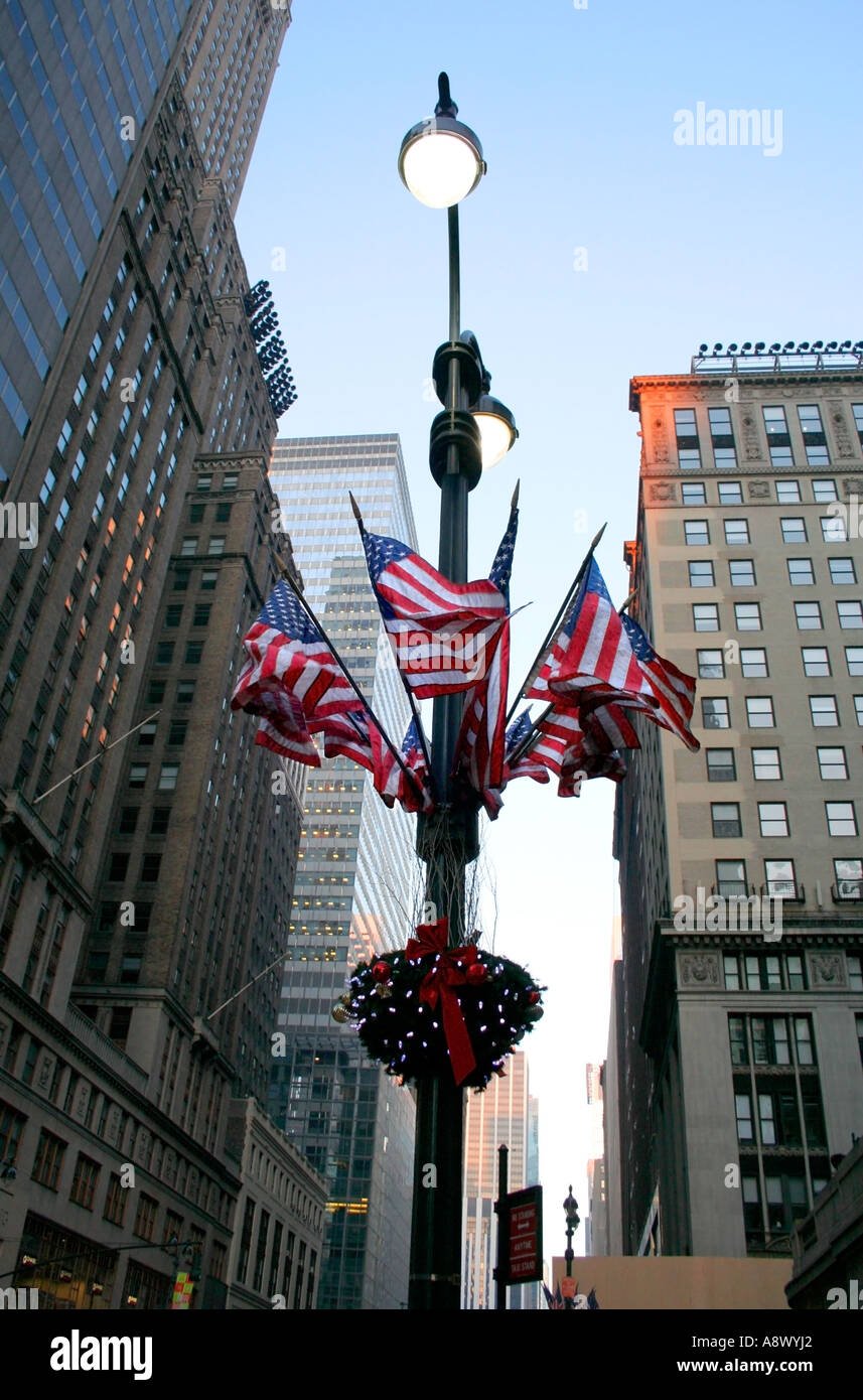 Amerikanische Flaggen am Laternenpfahl. New York City Straßenleuchten und Dekorationen. Hohen Gebäuden. Blauer Himmel. Am frühen Morgen im Winter. Stockfoto