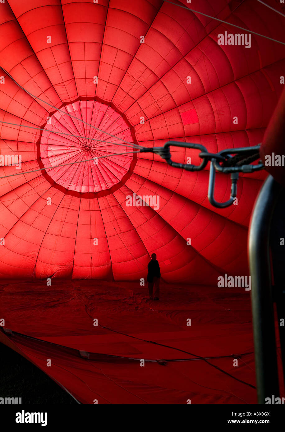 Mann, der während des Aufblasens von der Seite des Brenners aus in einen roten Heißluftballon läuft. Stockfoto