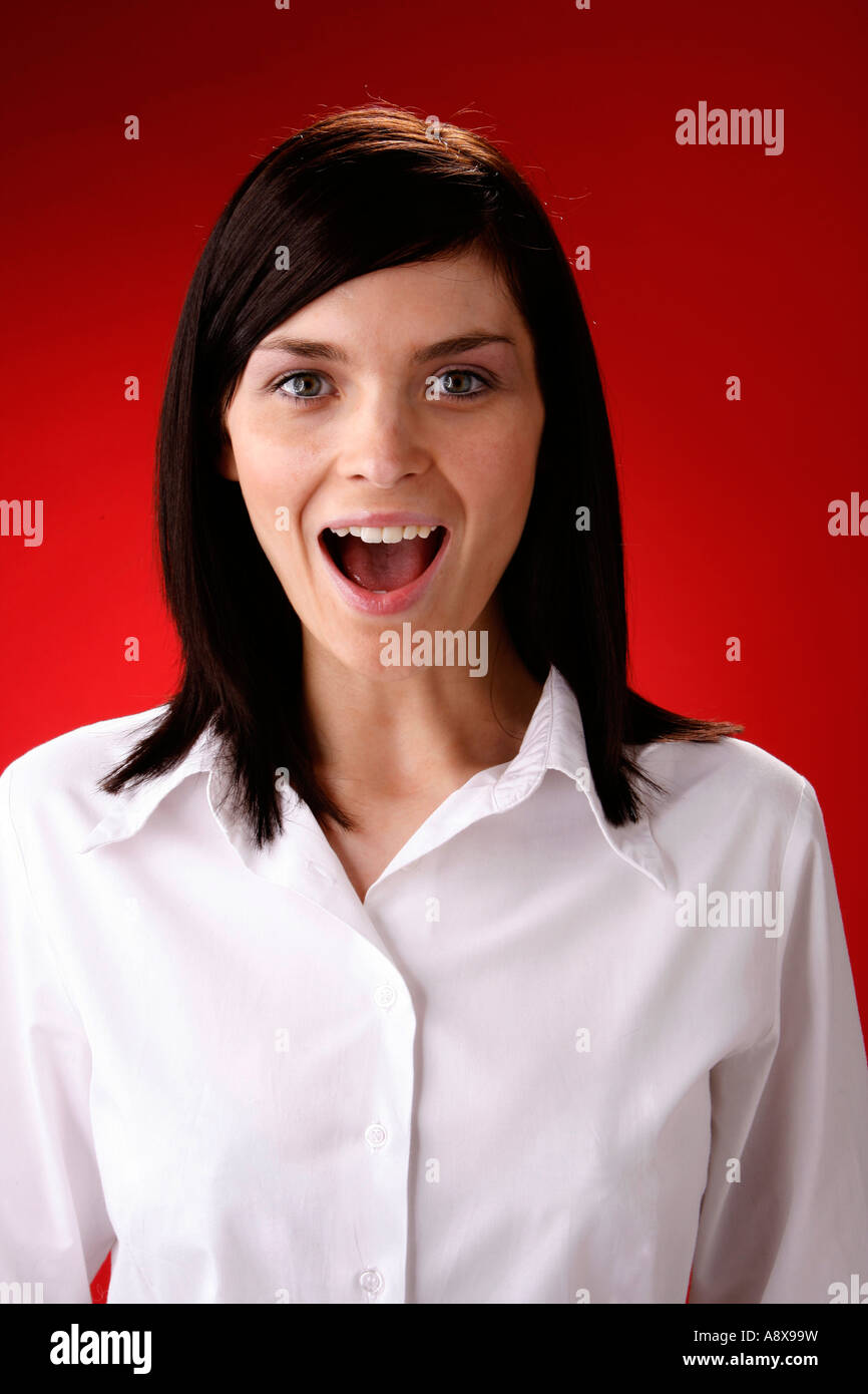 Hübsches junges Mädchen in weißen Bluse vor einem roten Hintergrund, überrascht lächelnd und Blick in die Kamera. Stockfoto