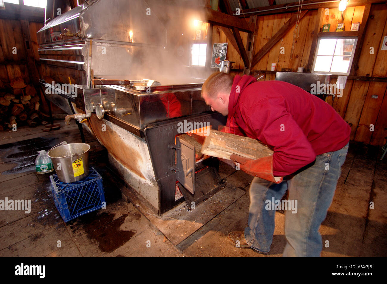 Ein Bauer arbeitet in einem traditionellen sugarhouse und kocht ahornsaft zu reinem Ahornsirup. Der Dampf steigt aus den großen Verdampferschalen, da der saft vorsichtig ist Stockfoto
