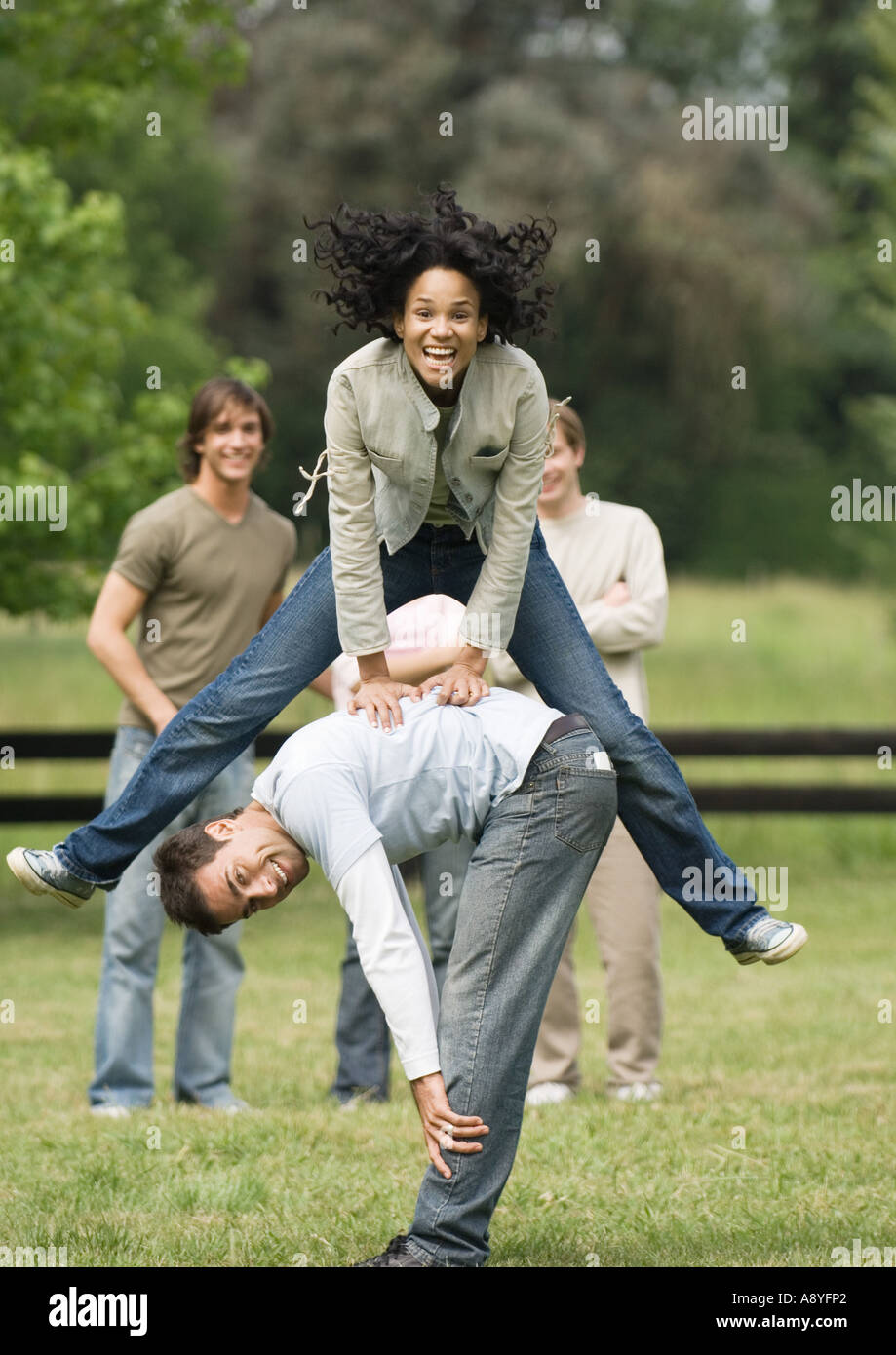 Junge Frau Bockspringen junger Mann zu spielen, während Freunde schauen auf Stockfoto