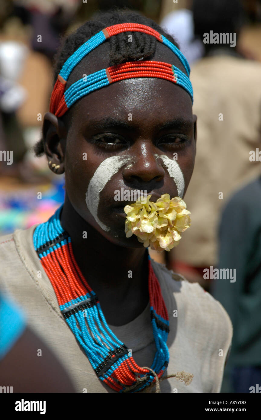 Junger Mann mit einer Blume in den Mund und bunte Halskette und Kopf Adorments Markt Keyafer Äthiopien Stockfoto