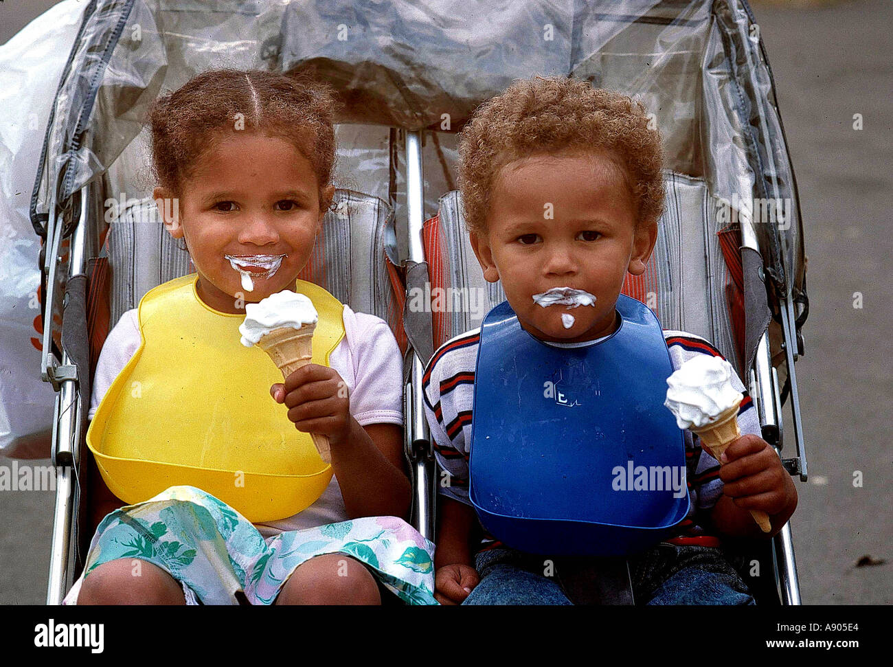 zwei Kleinkinder im Doppel Kinderwagen Eis essen Stockfoto