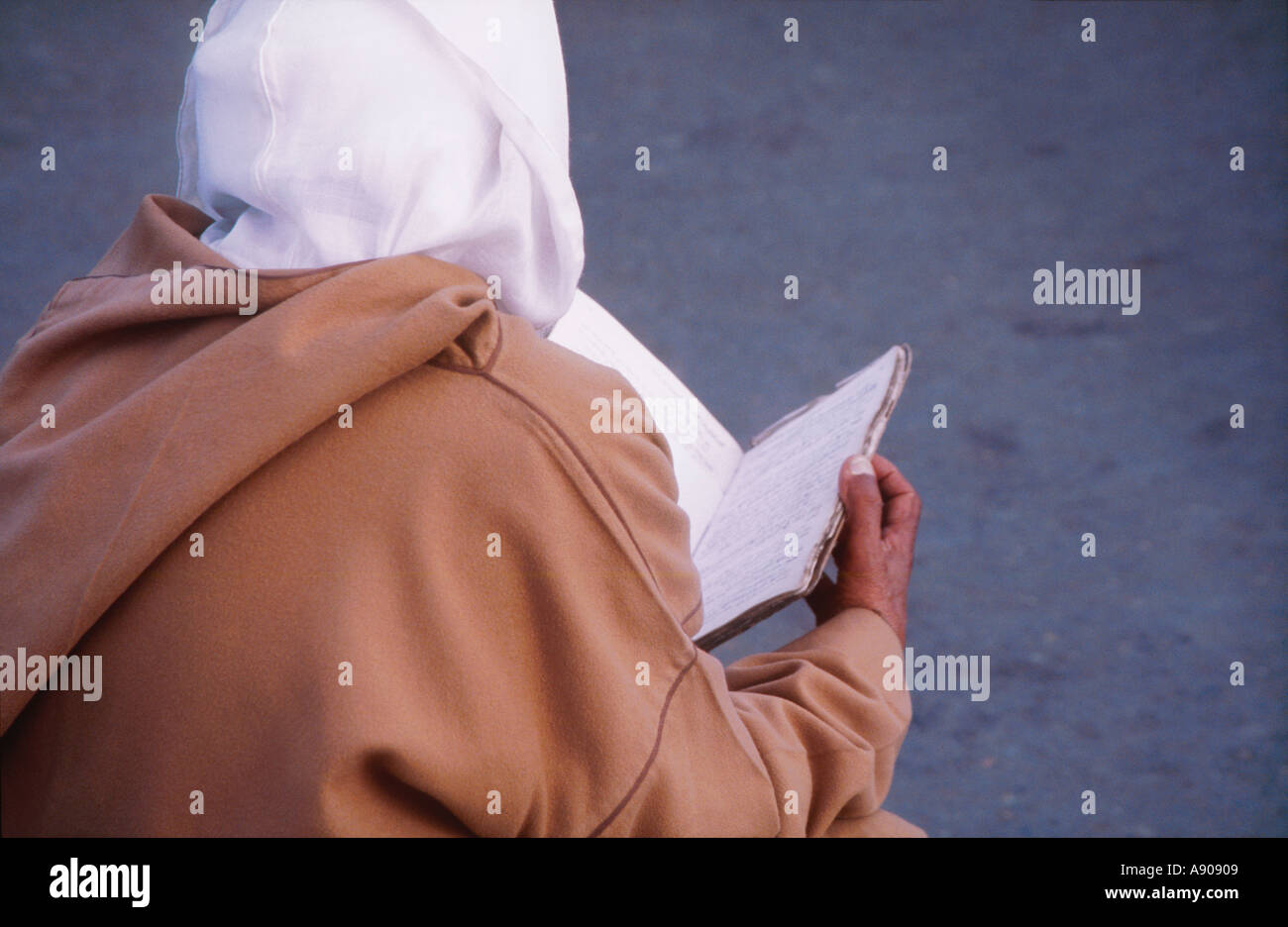 Mann in Kapuzen Kleid und Kopftuch in eine Stadt quadratische Marokko lesen Stockfoto