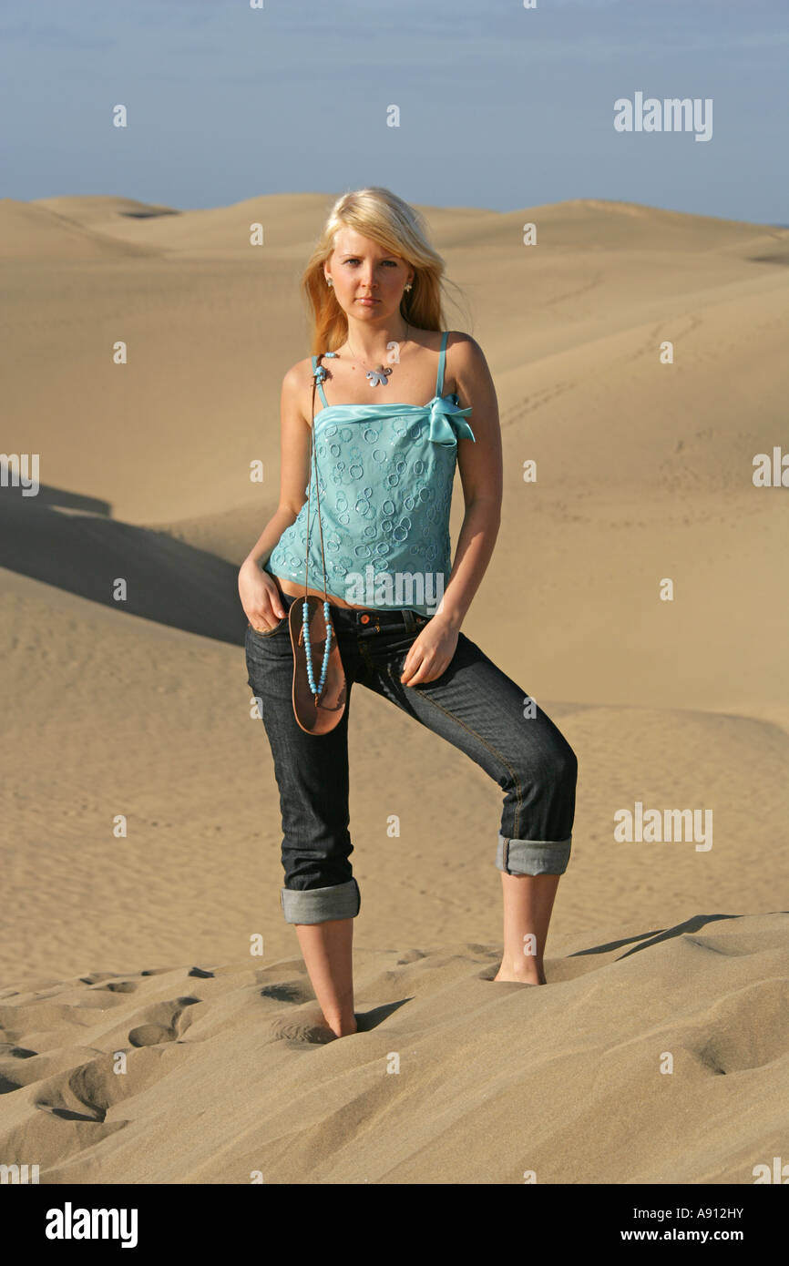Blondes Mädchen mit einem blauen Oberteil und Jeans auf Sanddünen stehen Stockfoto