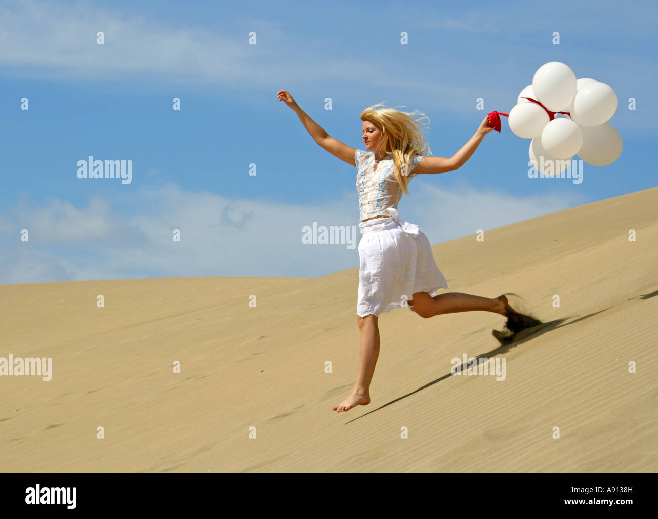 Blondes Mädchen mit einem Haufen weiße Luftballons auf Sanddünen Stockfoto