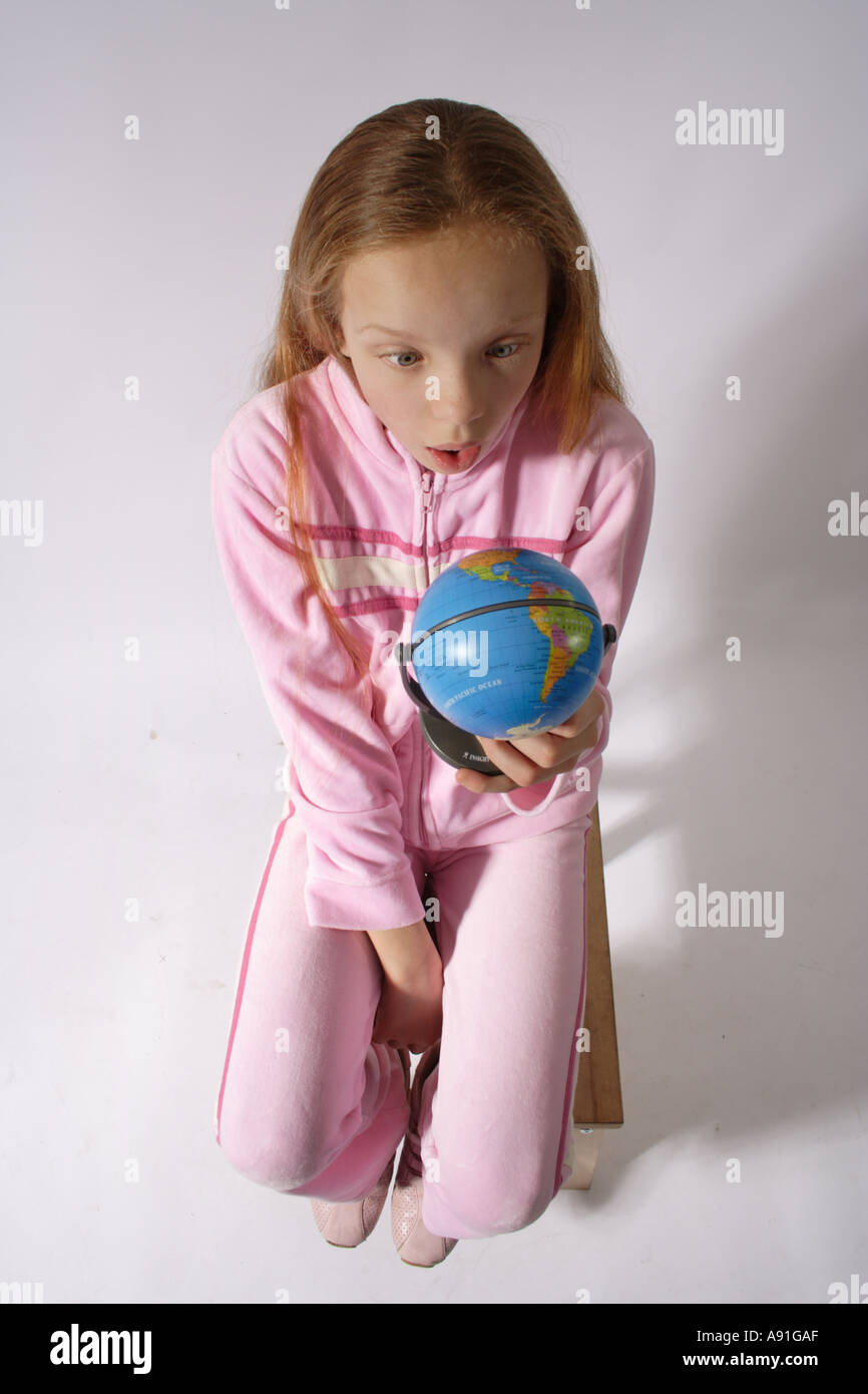 Junge Mädchen im Alter von 10 mit Blick auf einen Globus mit schockiert Pose sitzen Stockfoto