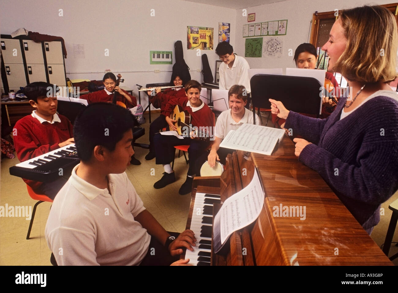 Musikunterricht im Klassenraum der Grundschule mit Schülern von 9-12 Jahren, die verschiedene Instrumente spielen, wobei eine begeisterte Lehrerin eine Probe durchführt Stockfoto