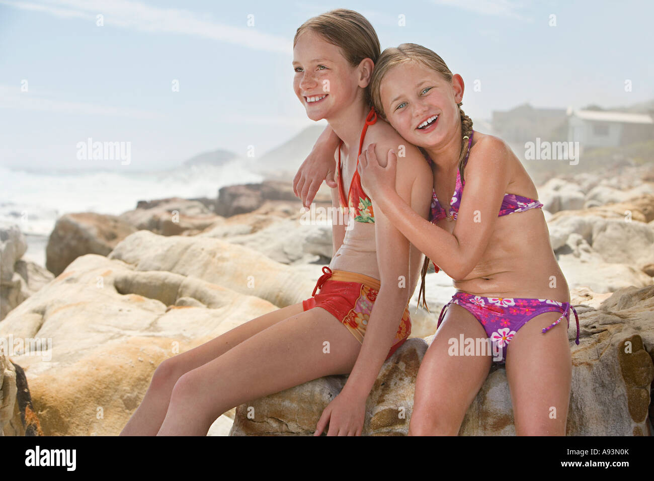 Zwei Mädchen (7-9, 10-12) sitzen auf Felsen am Strand Stockfoto