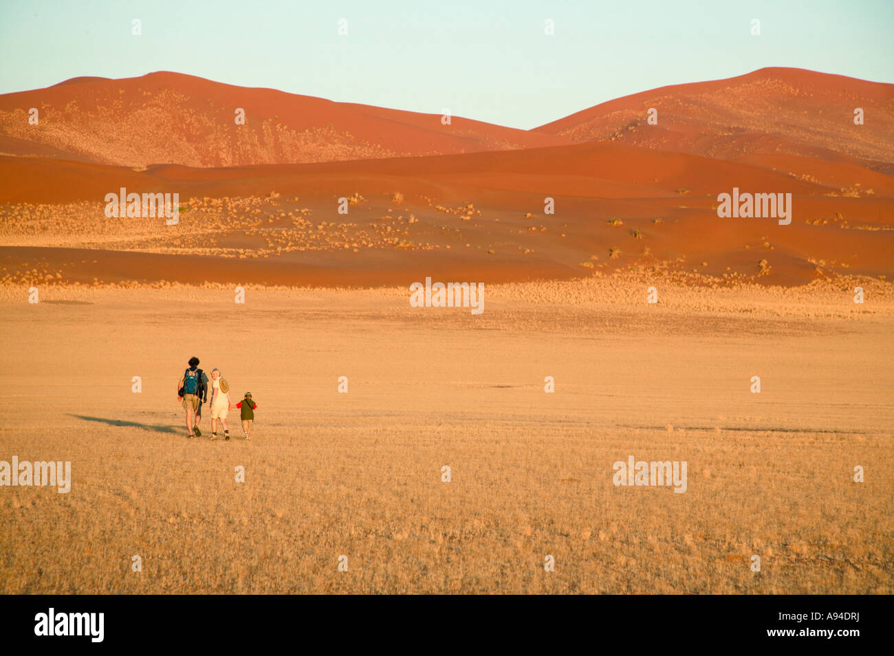 Szene mit drei Menschen, die zu Fuß von der Kamera entfernt und gegenüber einer Gruppe von massiven Dünen der Wüste Stockfoto