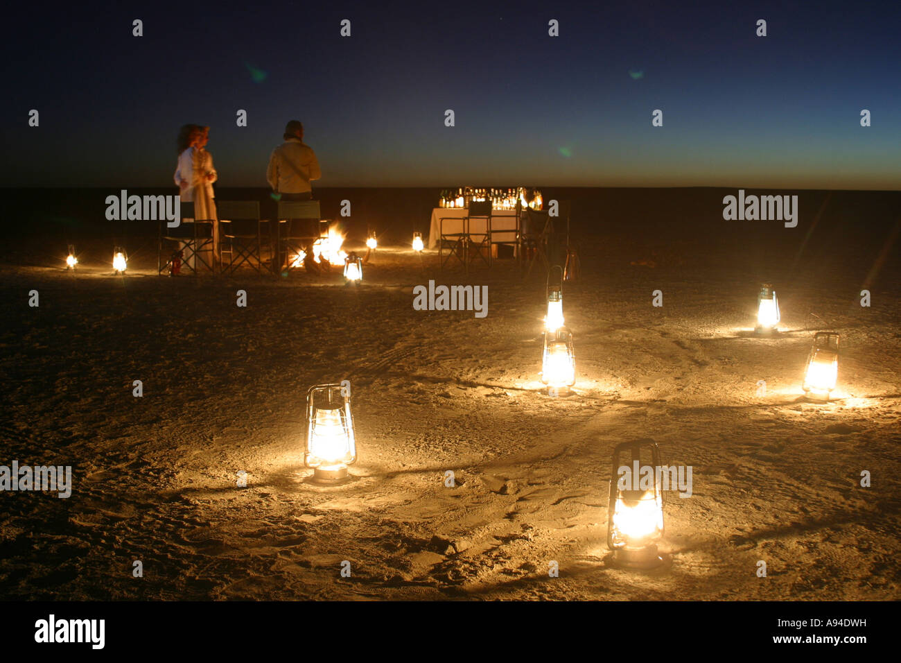 Ein Esstisch für Abendessen und mehrere hell beleuchteten Laternen, begib dich auf die staubige Oberfläche der Makgadikgadi Salzpfannen Botswana Stockfoto