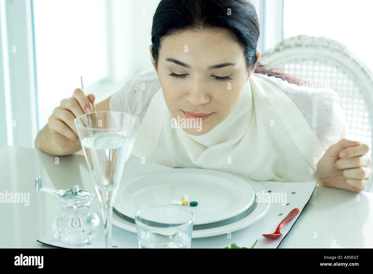 Trägerin am gedeckten Tisch sitzen Serviette um Hals, Vitamine auf Platte Stockfoto