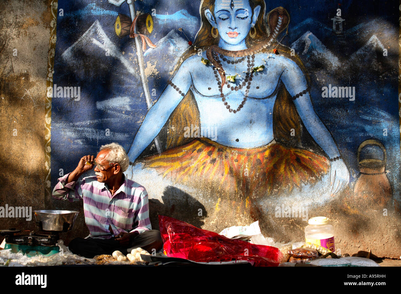 Indischer Mann, der Pooja-Artikel vor dem Wandbild von Shiva im Banganga Tank, Mumbai, Indien verkauft Stockfoto