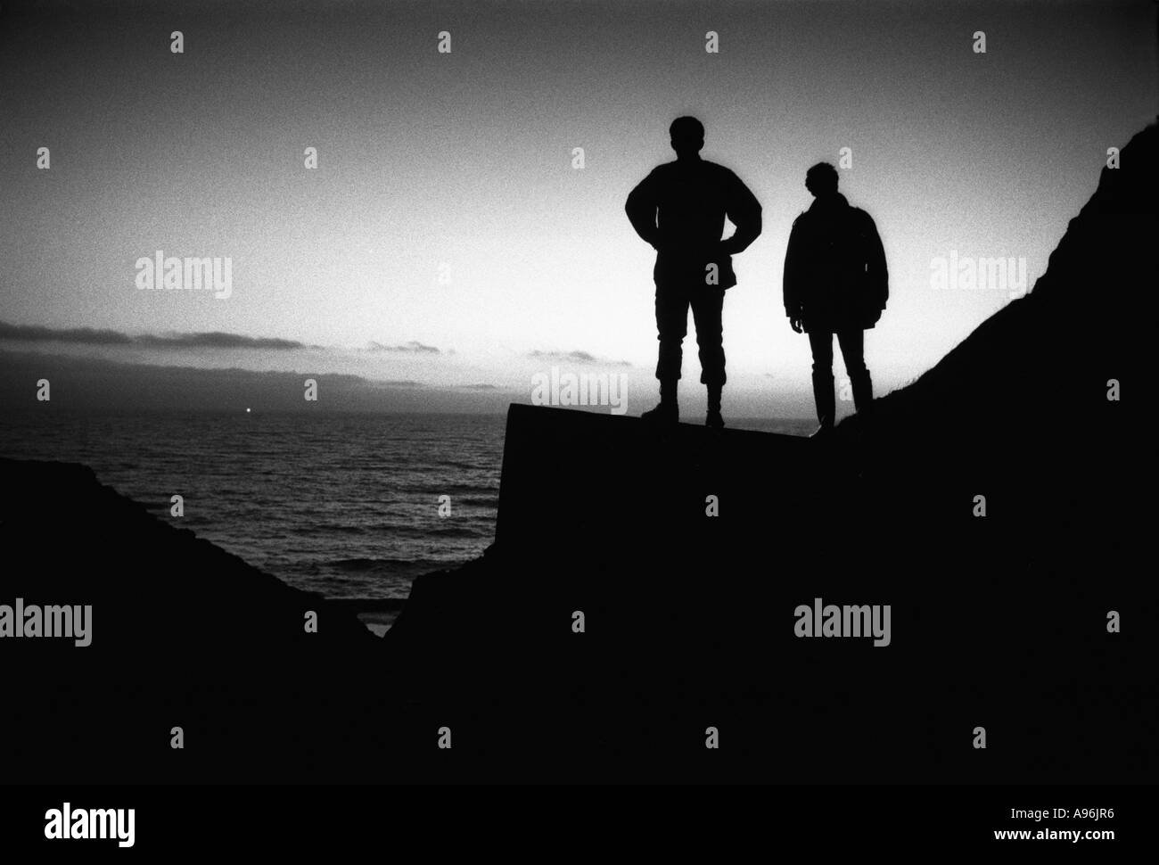 Zwei Männer stehen am zweiten Weltkrieg Pill Box Befestigungsanlagen in der Abenddämmerung mit Blick auf Meer bei Unidentifeid Licht am Horizont Stockfoto