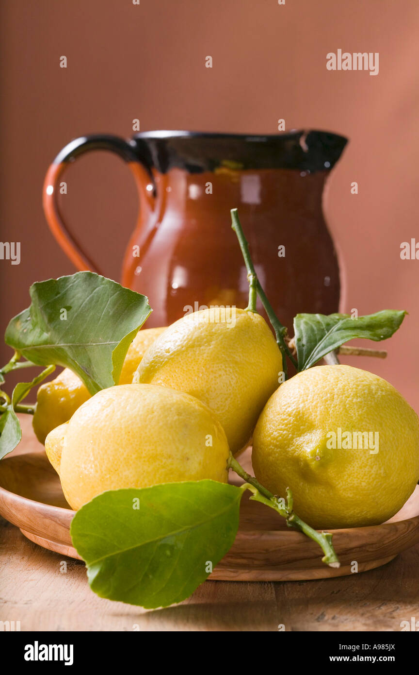 Frische Zitronen mit Blättern auf Platte vor Terrakotta Kanne FoodCollection Stockfoto