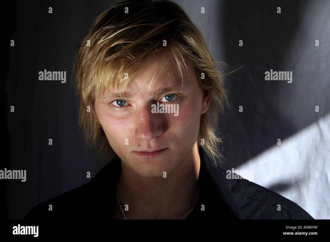 Nahaufnahme eines jungen Mannes mit blonden Haaren und intensiven blauen Augen, der direkt in die Kamera blickt, mit dramatischer Beleuchtung. Stockfoto
