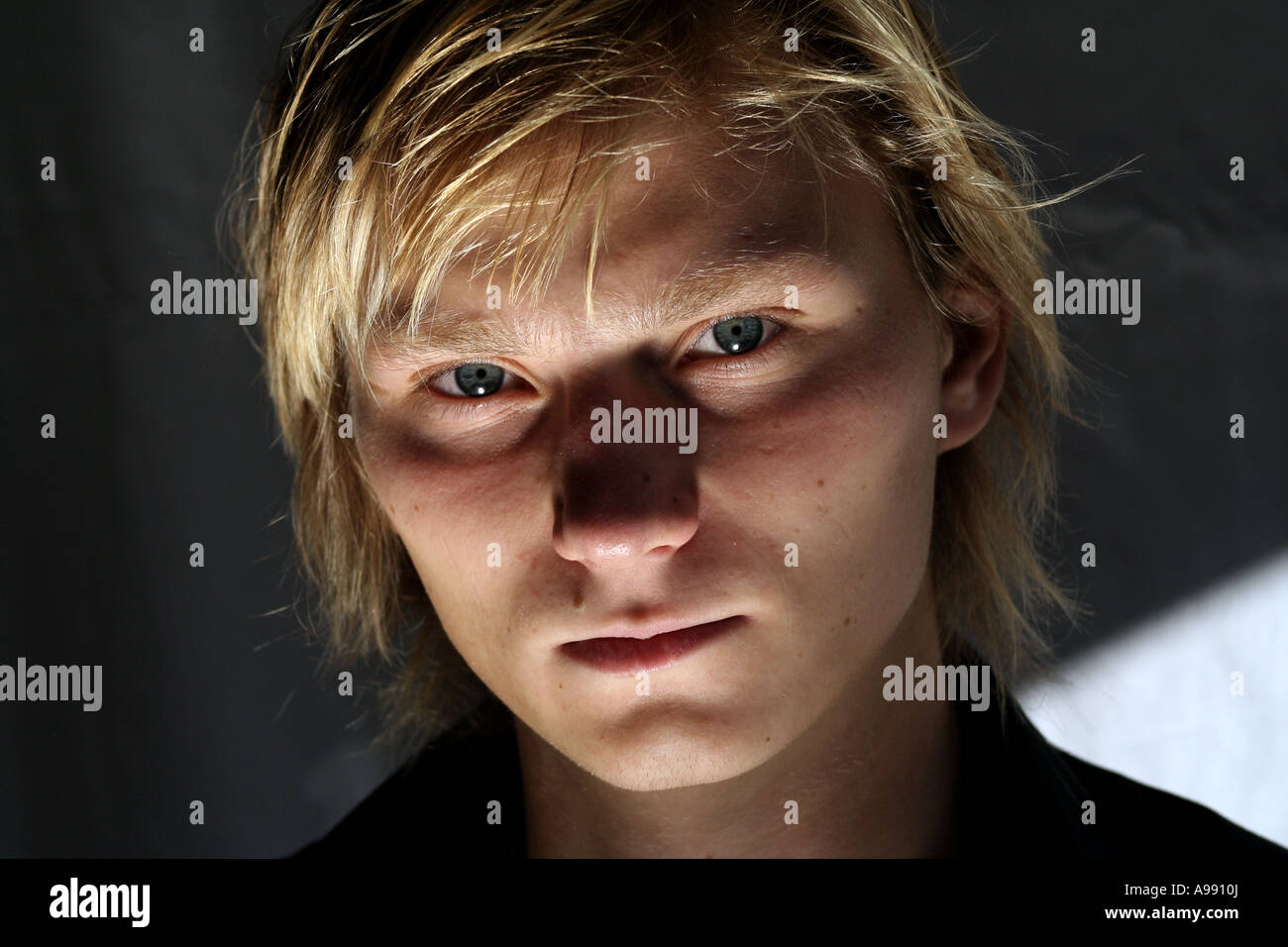 Nahaufnahme eines jungen Mannes mit blonden Haaren und intensiven blauen Augen, der direkt in die Kamera blickt, mit dramatischer Beleuchtung. Stockfoto