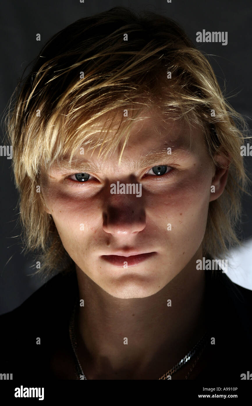Nahaufnahme eines jungen Mannes mit blonden Haaren und intensiven blauen Augen, der direkt in die Kamera blickt, mit dramatischer Beleuchtung. Stockfoto