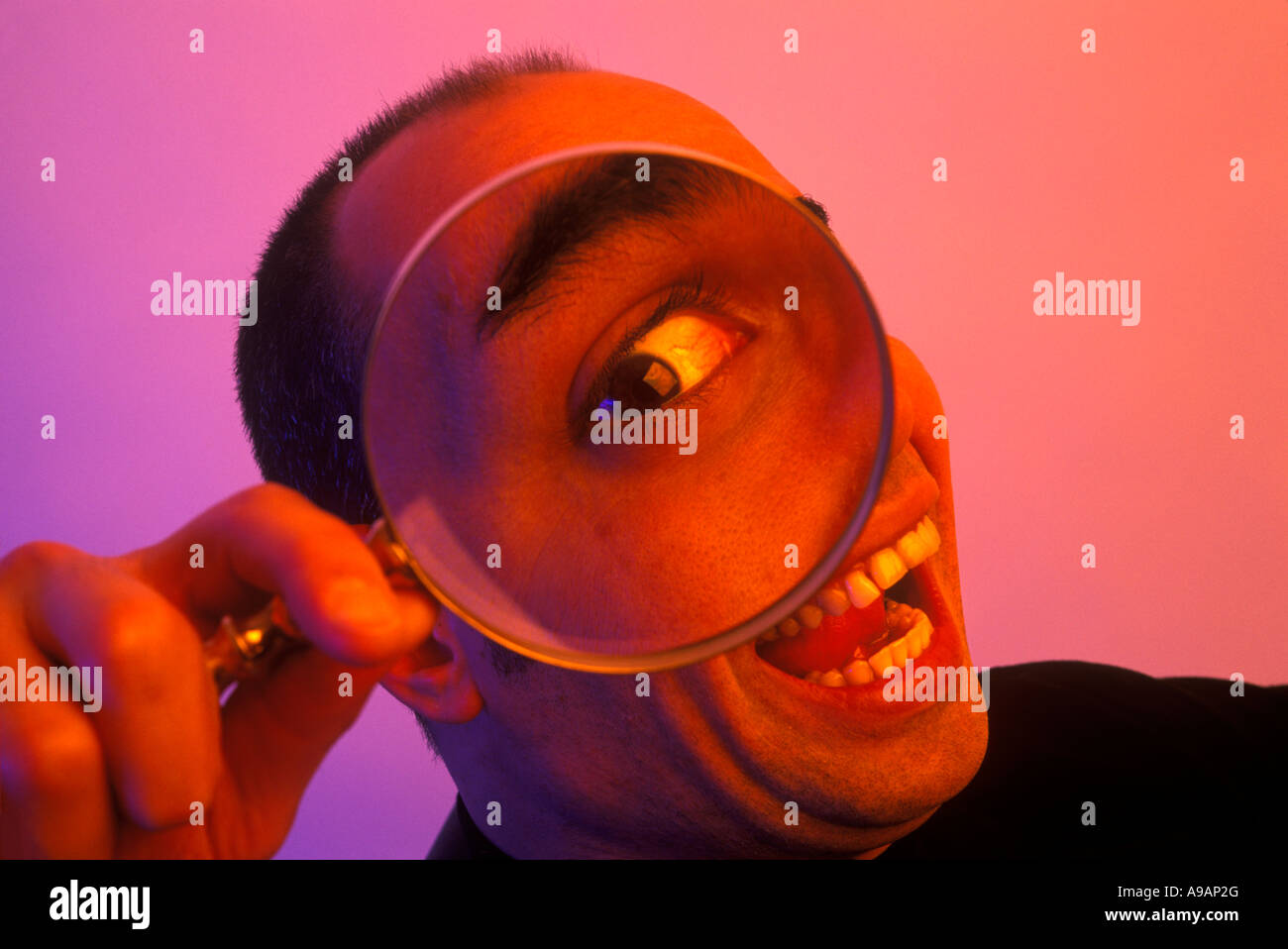 BIG EYE LÄCHELNDER MANN BLICK DURCH DIE LUPE Stockfoto