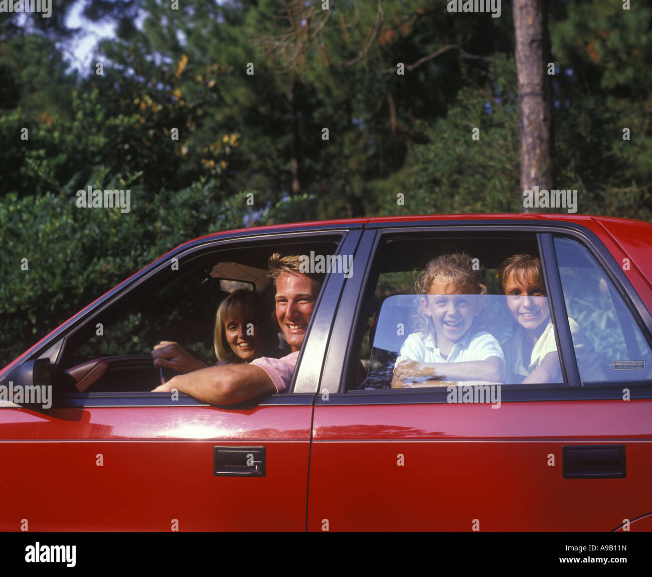 1990 HISTORISCHE GLÜCKLICH LÄCHELNDE KAUKASISCHE FAMILIE IM ROTEN AUTO SITZEN (©CHRYSLER CORP 1990) Stockfoto