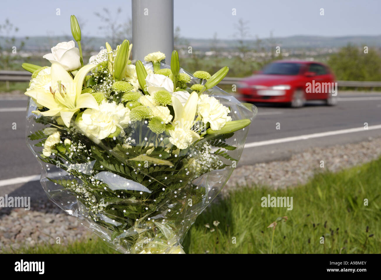 Auto beschleunigt vorbei ein floral Tribute Kennzeichnung der Stelle von einem tödlichen Verkehrsunfall Stockfoto