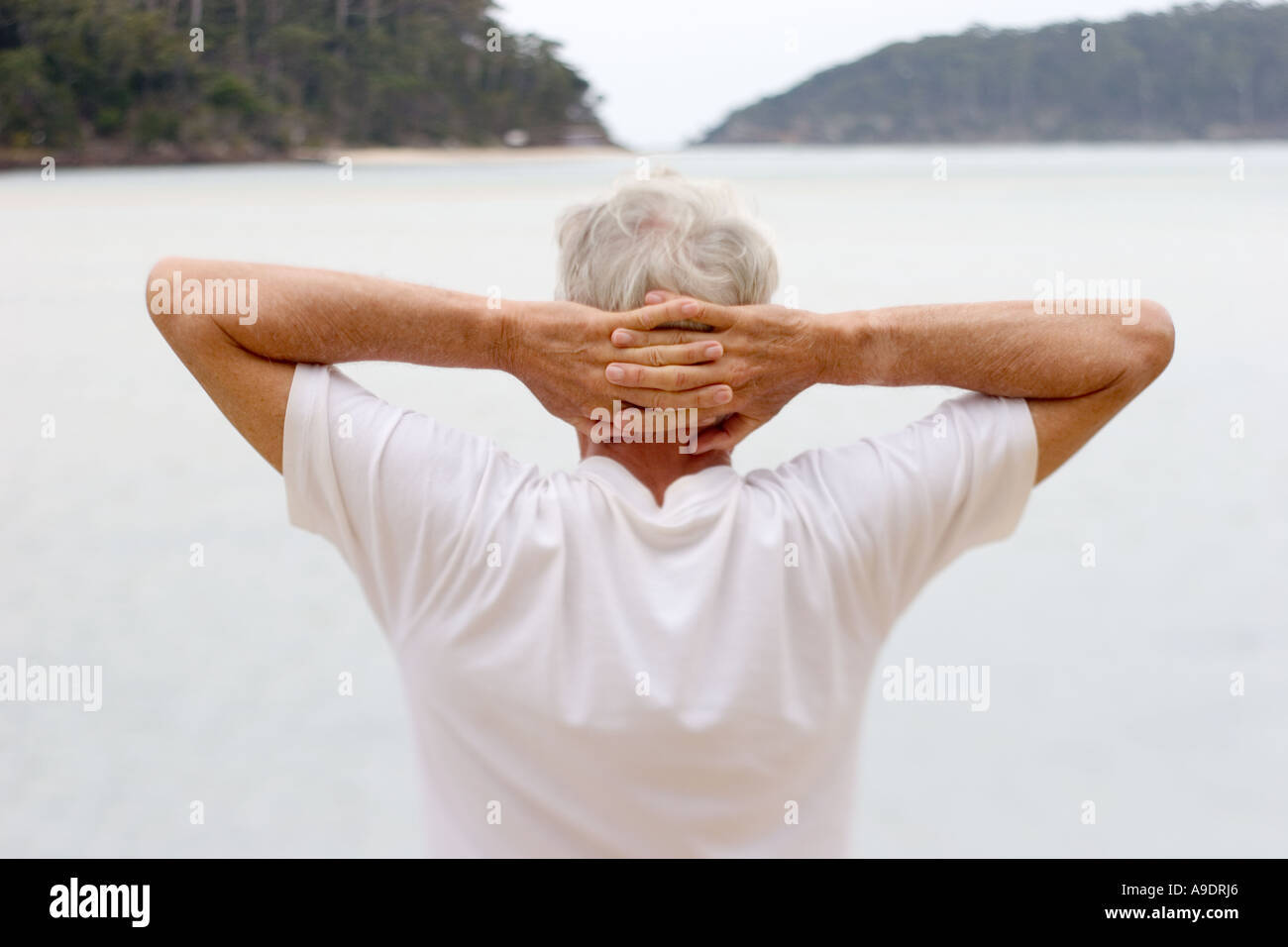 entspannte älterer Mann mit Händen hinter dem Kopf am Strand Stockfoto